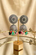 A pair of ornate silver-toned Indian jhumka earrings with colorful faceted bead drops, displayed on a gold stand.
