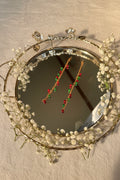 A pair of long gold-toned beaded jhumkha hair chains decorated with alternating red and green beads, displayed on a reflective silver tray.