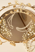 A pair of double-strand beaded jhumkha chain displayed on a decorative gold-toned mirror stand.