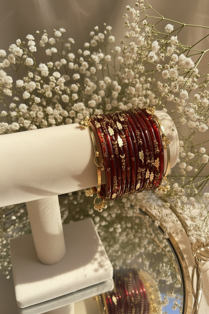 A set of red kashmiri bangles with gold foil patterns and gold-toned metal borders, displayed on a cream-colored jewelry stand.