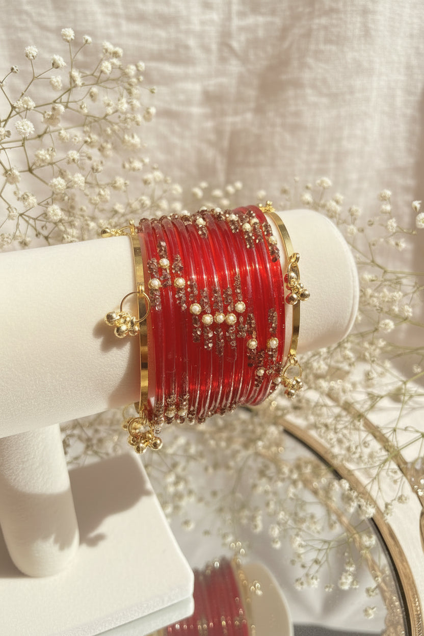 A set of red kashmiri bangles with gold-toned borders and beadwork, displayed on a cream-colored jewelry stand.