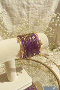 A stack of purple kashmiri bangles with gold floral and dot embellishments displayed on a cream-colored jewelry stand.