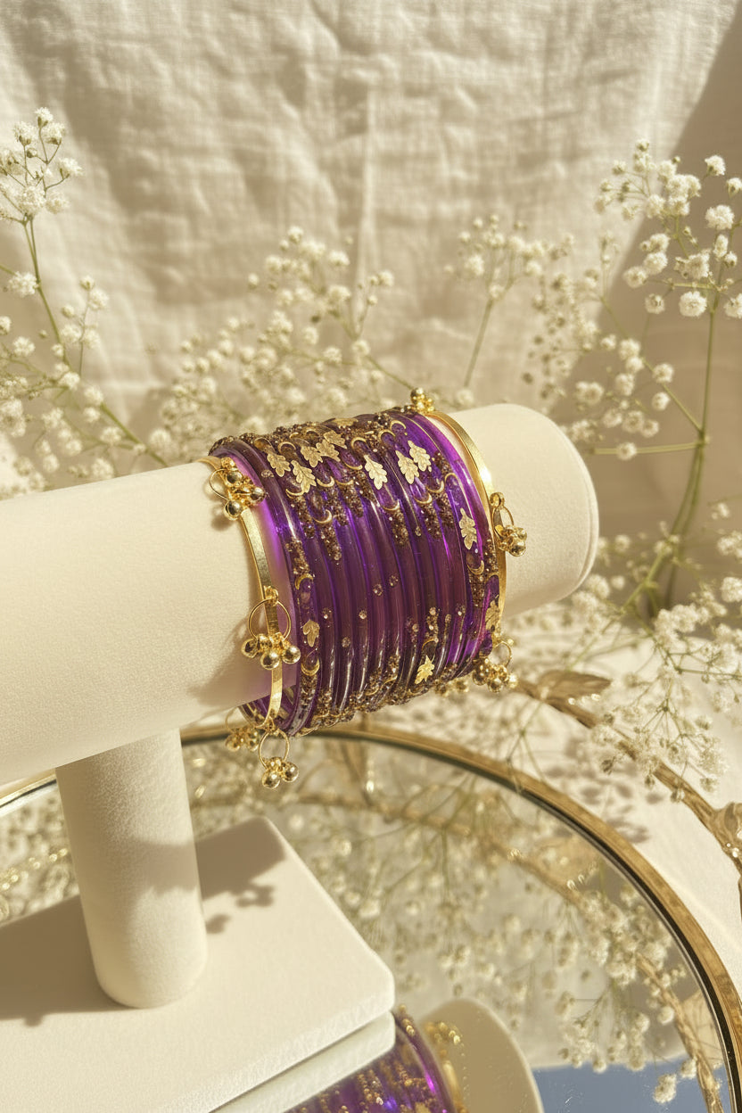 A stack of purple kashmiri bangles with gold floral and dot embellishments displayed on a cream-colored jewelry stand.