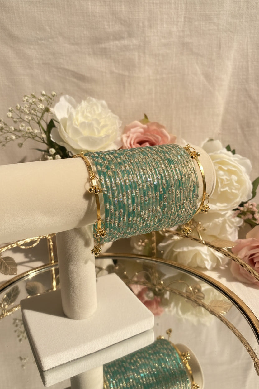 A close-up of a turquoise and silver kashmiri bangels displayed on a white jewelry stand, with gold-toned bangles and decorative beads visible around it.
